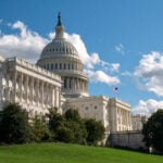 U.S. Capitol building on a sunny day with blue sky in background and lawn in foreground.