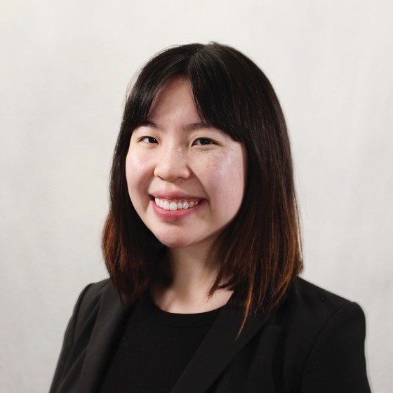 Headshot of Anya Fang, smiling, looking at camera, in front of gray background.