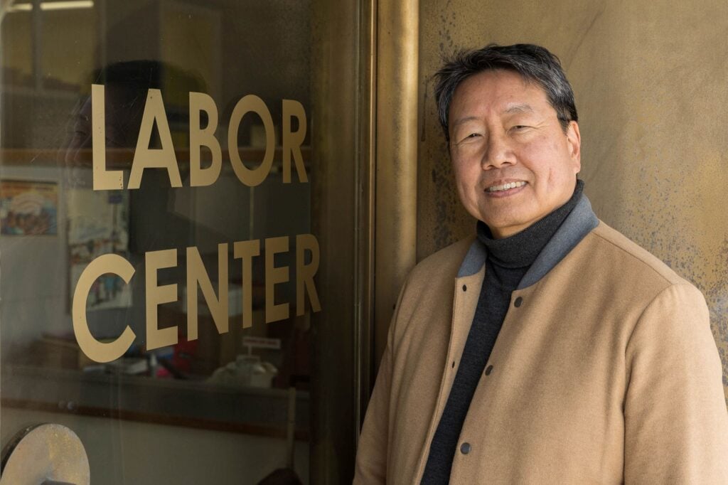 Photo of Kent Wong, looking into the camera and smiling, in front of a sign reading "Labor Center.